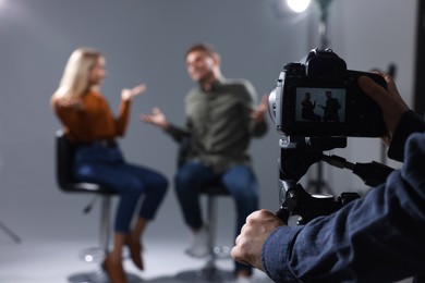Photo of Casting call. Man and woman performing while camera operator filming them against grey background in studio, selective focus