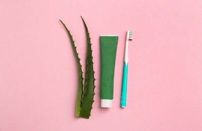 Photo of Tube of toothpaste, toothbrush and fresh aloe on pink background, flat lay