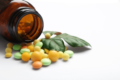 Photo of Bottle with vitamin pills and green leaves on white background, closeup