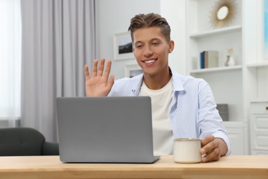 Photo of Happy young man having video chat via laptop at wooden table indoors