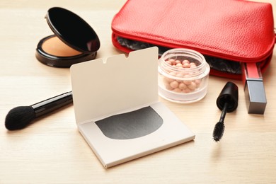 Photo of Facial oil blotting tissues and different decorative cosmetics on wooden table. Mattifying wipes