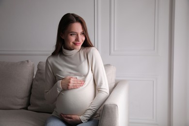 Photo of Young pregnant woman sitting on sofa at home. Space for text