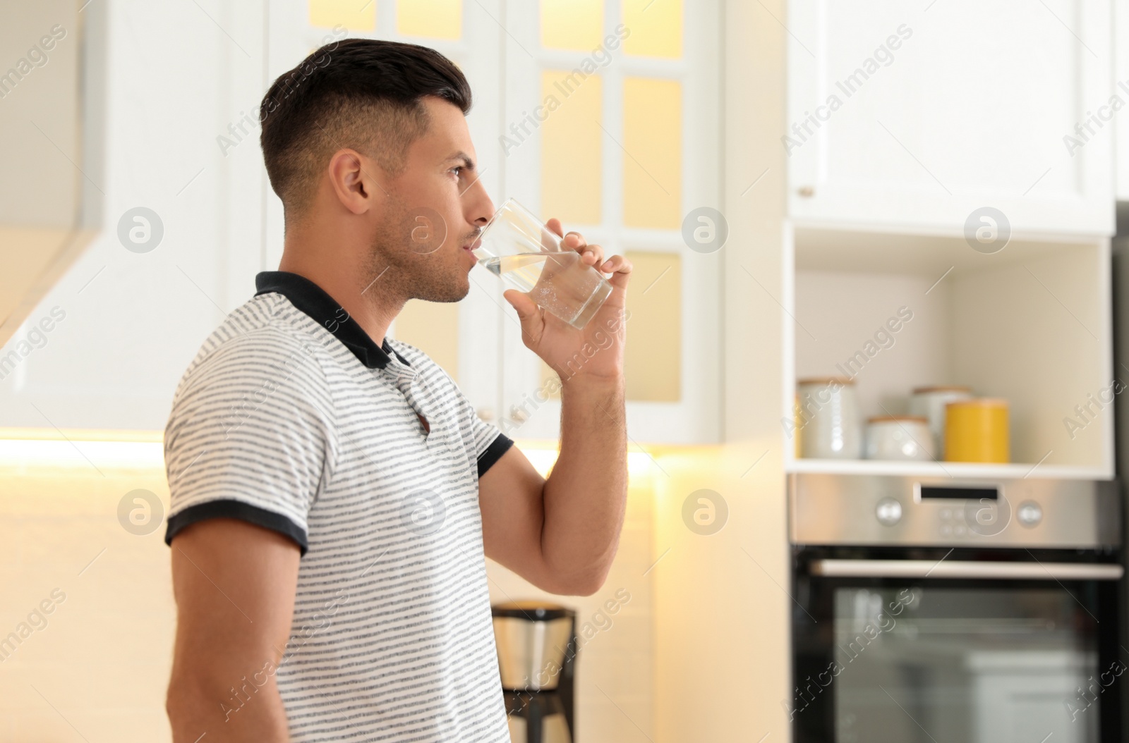 Man drinking pure water from glass in kitchen. Space for text Photo of Man drinking pure water from glass in kitchen. Space for text