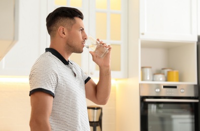 Photo of Man drinking pure water from glass in kitchen. Space for text