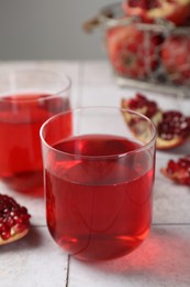 Photo of Tasty pomegranate juice in glasses and fresh fruits on white tiled table, closeup