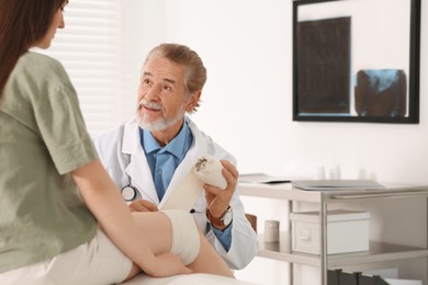 Photo of Orthopedist applying bandage onto patient's knee in clinic