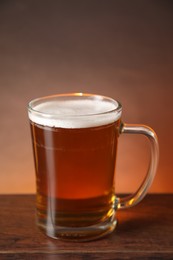 Photo of Mug with fresh beer on wooden table against brown background