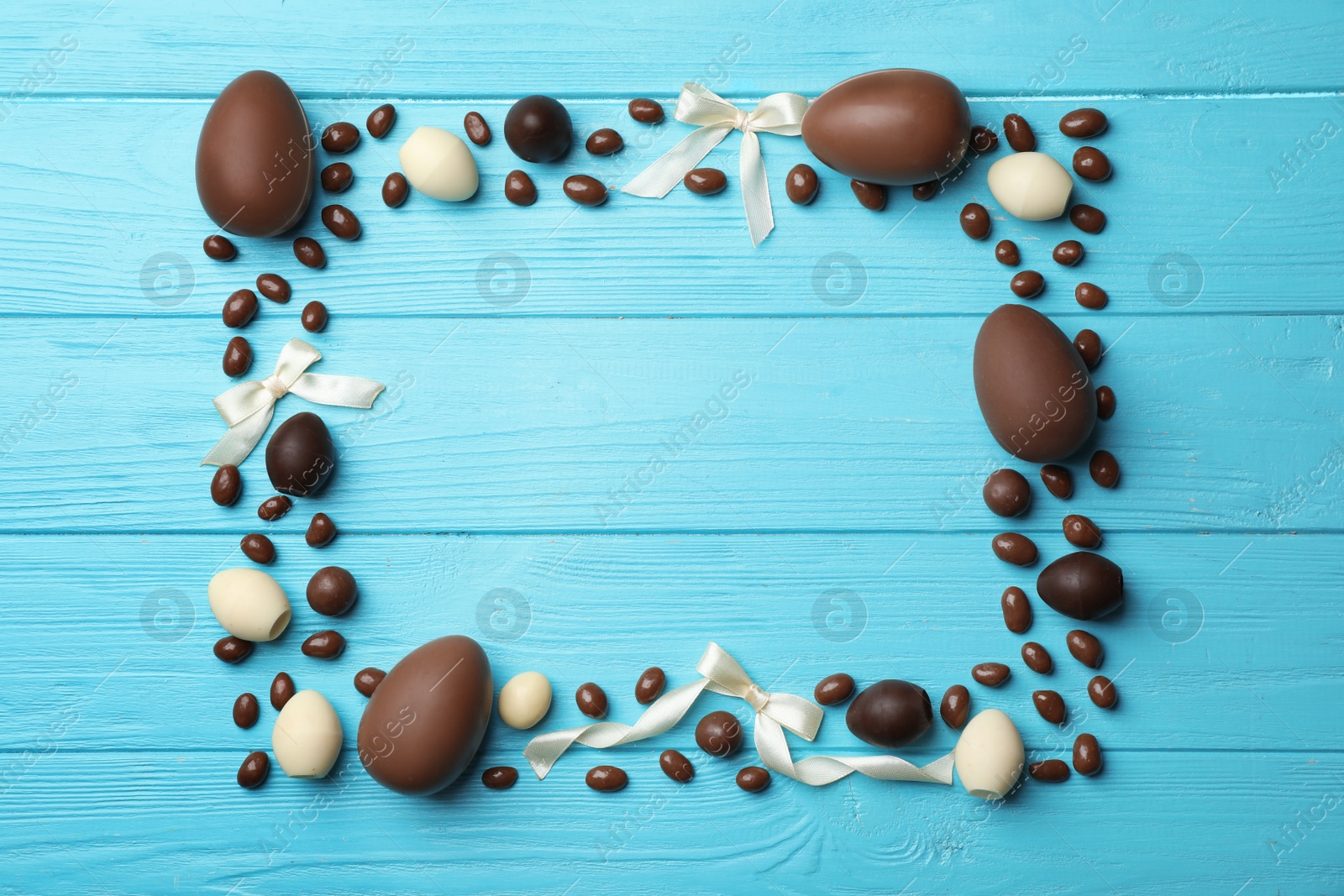 Photo of Frame made of chocolate Easter eggs on color wooden background, top view with space for text