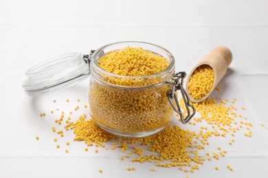 Photo of Millet groats in glass jar and scoop on white tiled table
