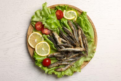 Photo of Tray with delicious fried anchovies, lemon slices, cherry tomatoes and lettuce leaves on white wooden table, top view
