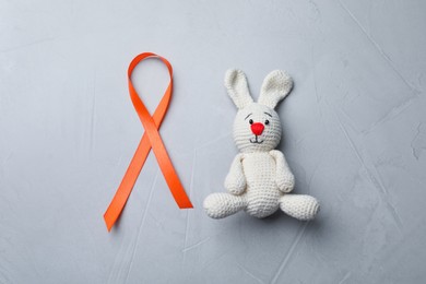 Photo of Orange ribbon and toy bunny on light grey table, flat lay. Multiple sclerosis awareness