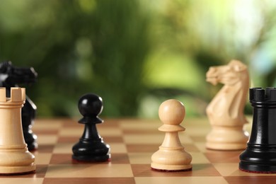 Photo of Wooden chess pieces on game board against blurred background, closeup