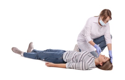 Photo of Doctor in uniform and protective mask performing first aid on unconscious woman against white background