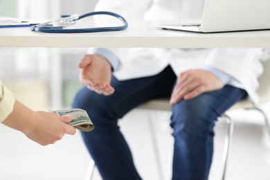 Photo of Patient giving bribe to doctor under table in clinic, closeup. Corrupted medicine