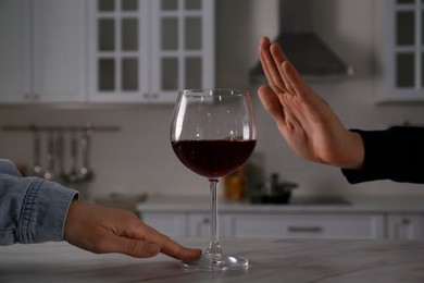 Photo of Man refusing to drink red wine in kitchen, closeup. Alcohol addiction treatment
