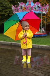 Photo of Happy little girl with colorful umbrella standing in puddle outdoors