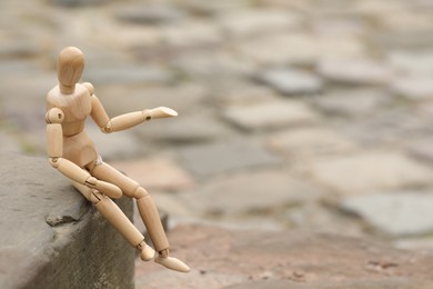 Photo of Wooden human figure sitting on curb outdoors, space for text