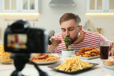 Photo of Food blogger recording eating show on camera in kitchen. Mukbang vlog