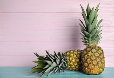 Photo of Fresh ripe juicy pineapples on light blue wooden table. Space for text