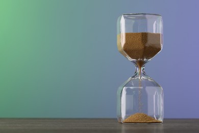 Photo of Hourglass with flowing sand on table against color background, space for text