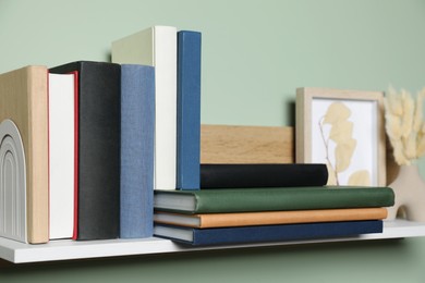 Photo of Wooden shelf with many hardcover books, picture and dry flowers on light green wall