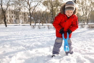 Photo of Cute little boy playing with snowball maker in park on sunny winter day. Space for text