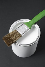 Photo of Can of white paint with brush on black background