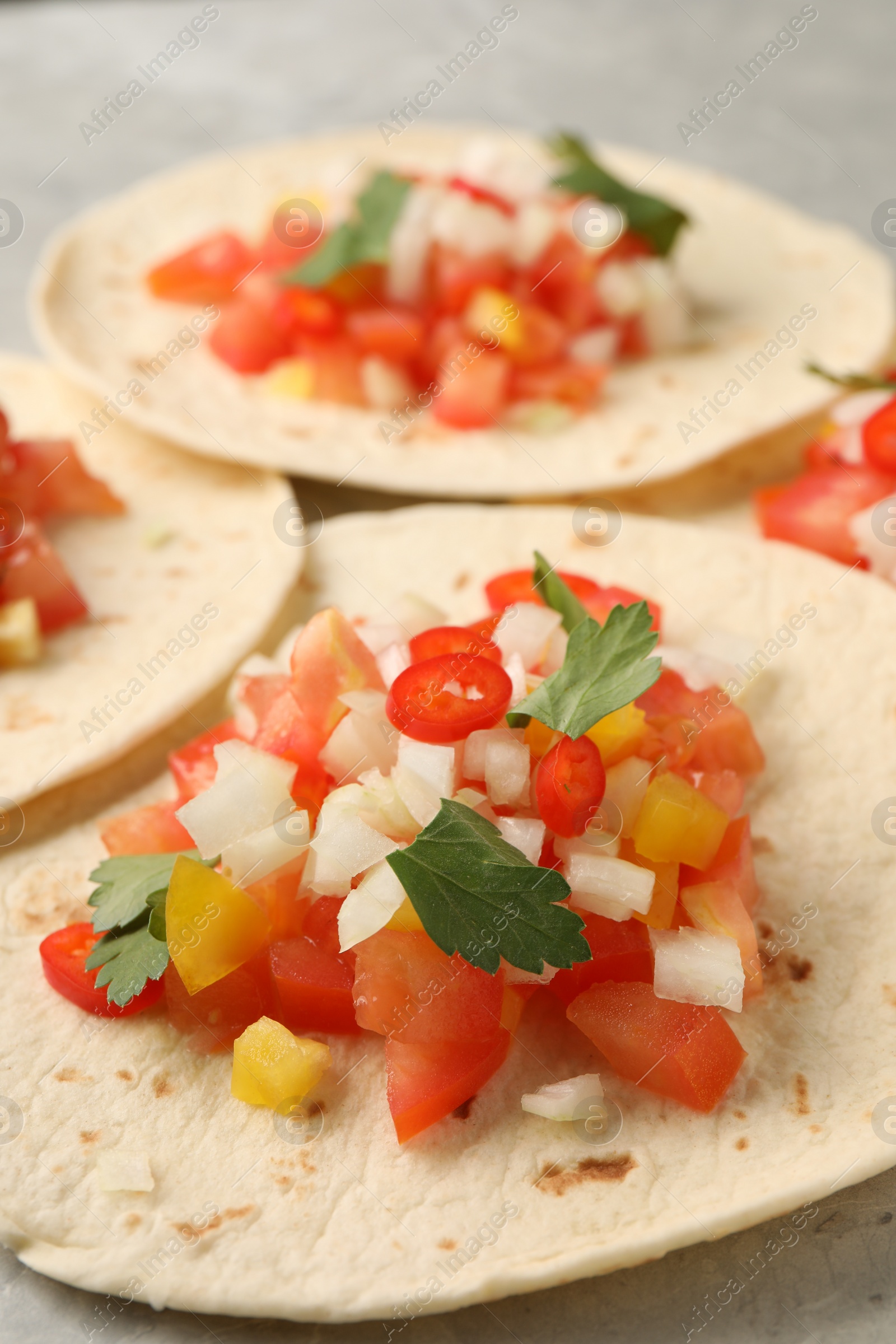 Photo of Delicious tacos with vegetables and parsley on grey table, closeup