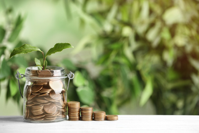 Photo of Coins and green sprout on white wooden table against blurred background, space for text. Money savings