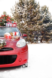 Photo of Car with Christmas tree, wreath and gifts in snowy forest on winter day. Space for text