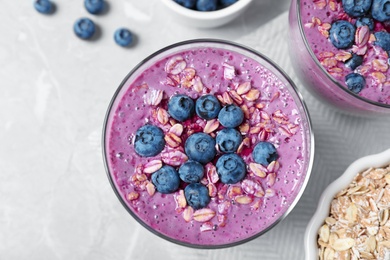 Photo of Glass of tasty blueberry smoothie with muesli on grey marble table, flat lay