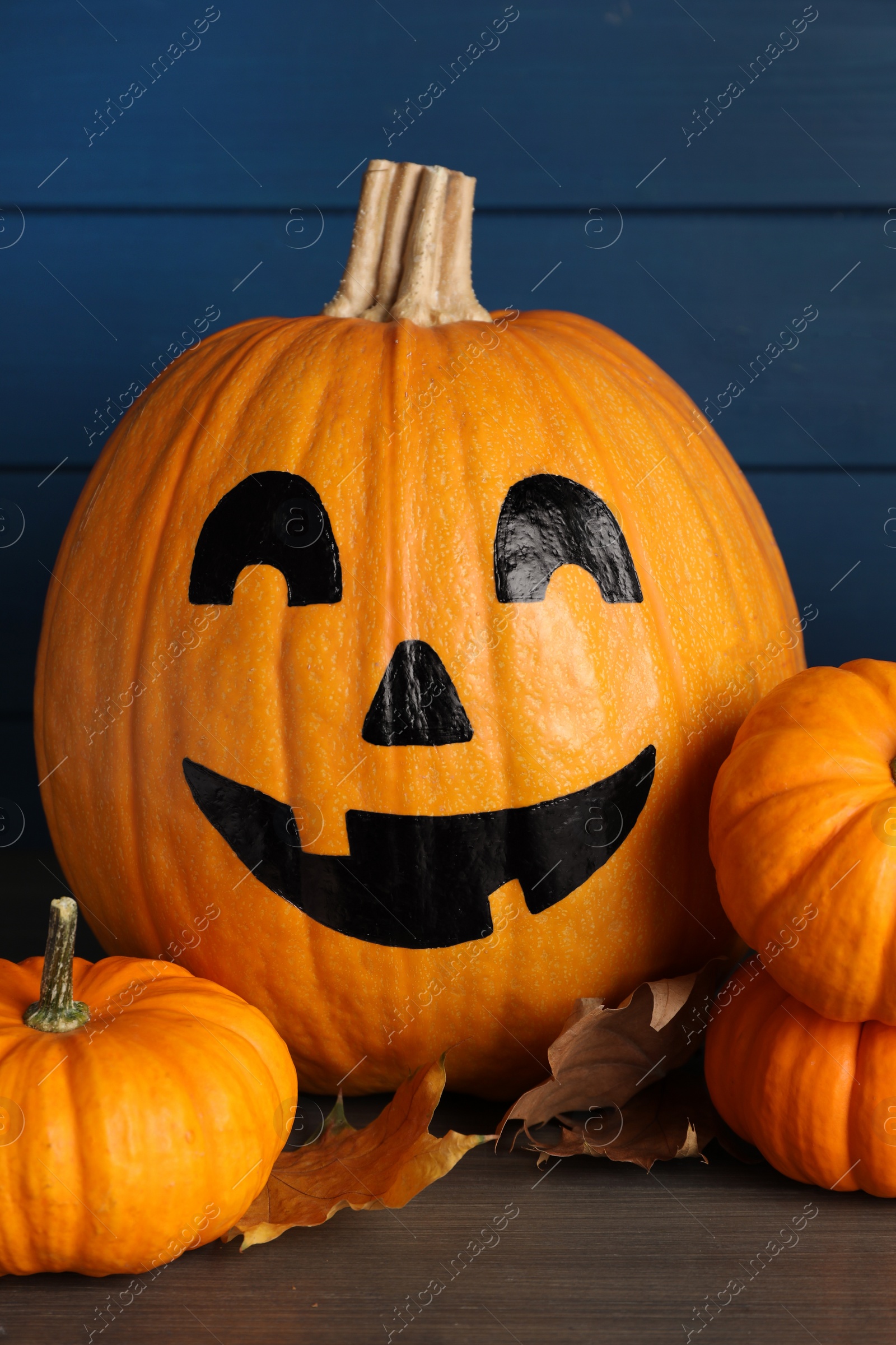 Photo of Orange pumpkins and one with drawn spooky face on wooden table. Halloween celebration