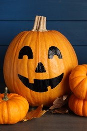 Photo of Orange pumpkins and one with drawn spooky face on wooden table. Halloween celebration