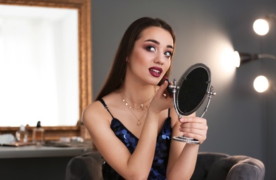Portrait of beautiful woman applying makeup indoors