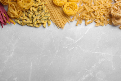 Photo of Different types of pasta on light grey marble table, flat lay. Space for text