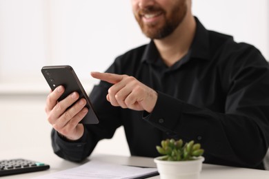 Photo of Smiling man using smartphone at table in office, closeup