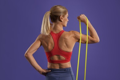 Photo of Athletic woman exercising with elastic resistance band on purple background, back view