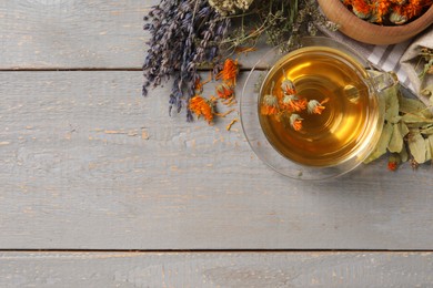 Photo of Freshly brewed tea and dried herbs on grey wooden table, flat lay. Space for text