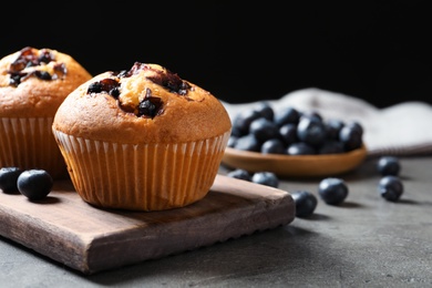 Photo of Wooden board with blueberry muffins on grey table against black background, closeup view. Space for text