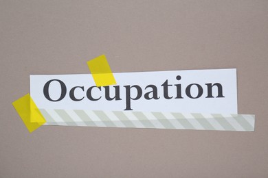 Photo of Word Occupation attached with yellow adhesive tape on grey background