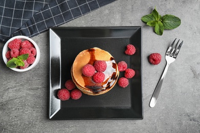 Photo of Tasty pancakes with raspberries served on grey table, flat lay