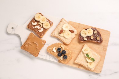 Photo of Toasts with different nut butters, fruits and nuts on white marble table, flat lay