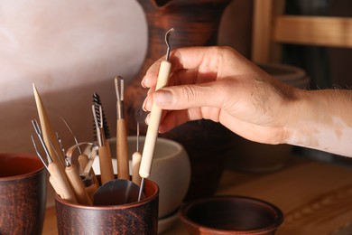 Photo of Woman taking clay crafting tool from cup in workshop, closeup