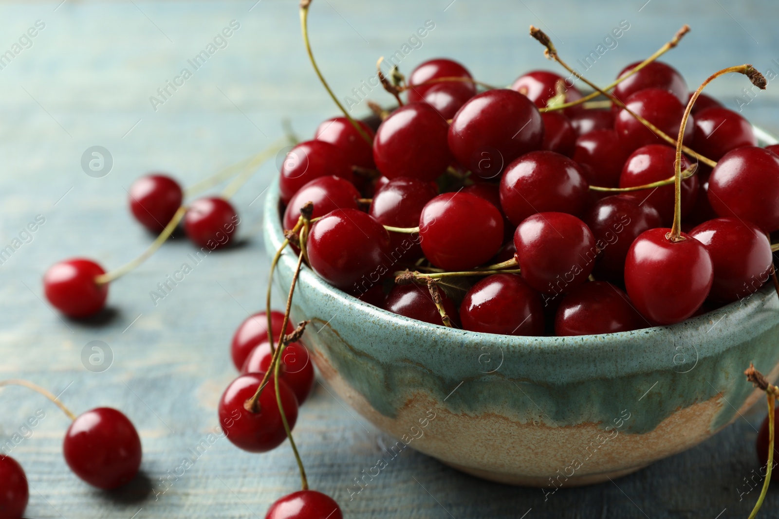 Photo of Bowl of delicious cherries on blue wooden table, closeup view. Space for text