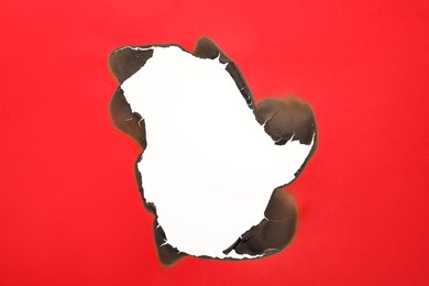 Photo of Burnt hole in red paper on white background, space for text