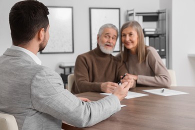 Photo of Elderly couple consulting insurance agent about pension plan at wooden table indoors