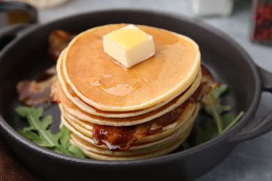 Photo of Tasty pancakes with butter, fried bacon and fresh arugula on grey table, closeup