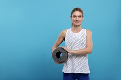 Photo of Sportswoman with fitness mat on light blue background, space for text