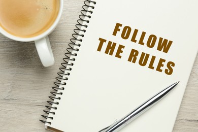 Image of Notebook with phrase Follow The Rules, pen and cup of coffee on wooden table, flat lay