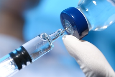 Photo of Doctor filling syringe with vaccine from vial on blue background, closeup